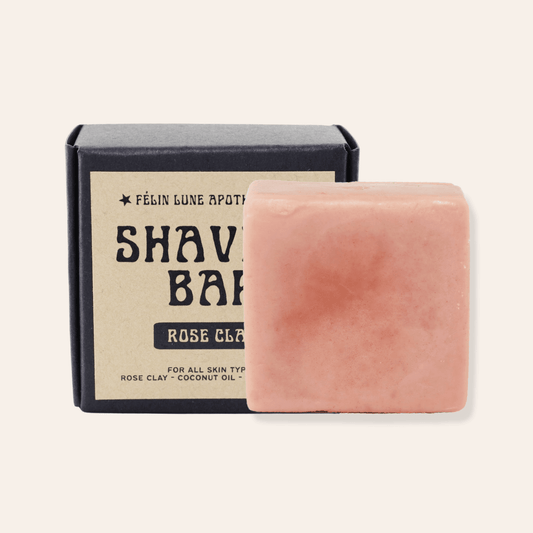 A pink solid shaving bar in front of a black box with a kraft label. The label reads Felin Lune Apothecary Shaving Bar Rose Clay.