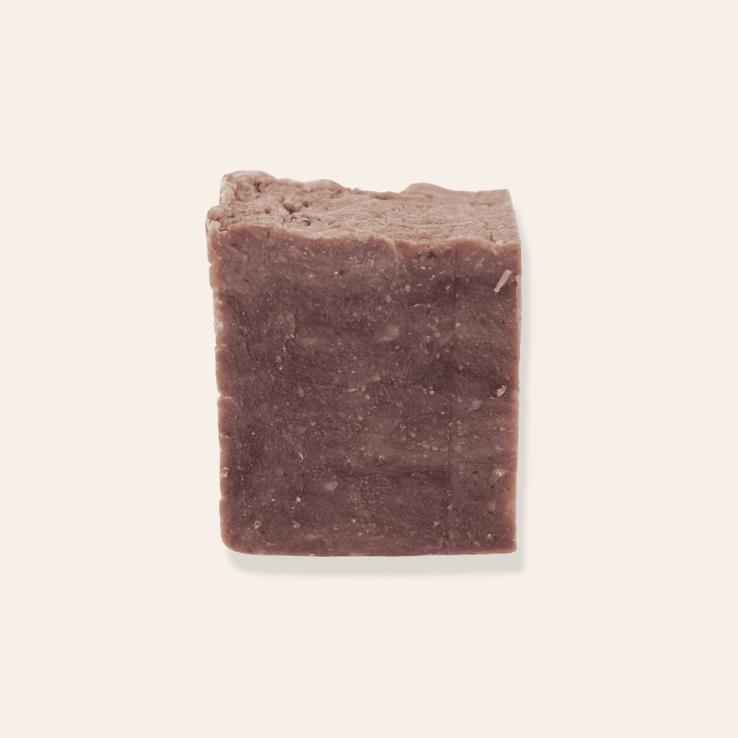 A bar of brown natural coconut milk soap on a cream background.