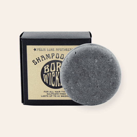 A round black shampoo bar set in front of a black box and kraft label.