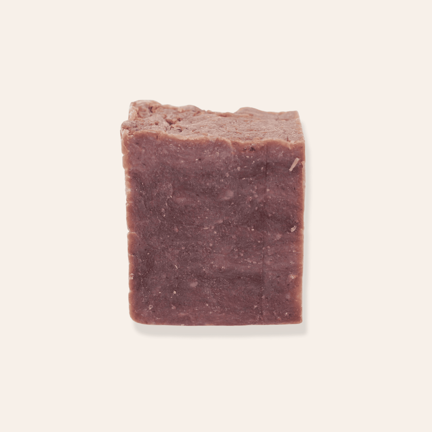 A bar of brick red natural coconut milk soap on a cream background.