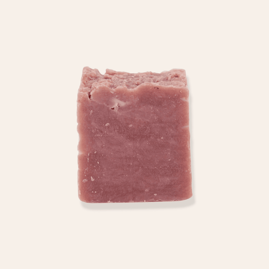 A bar of pink natural coconut milk soap on a cream background.