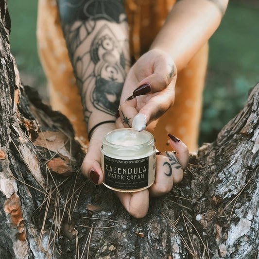 A hand holding a jar of Calendula Water Cream with a finger that has been dipped into the cream.